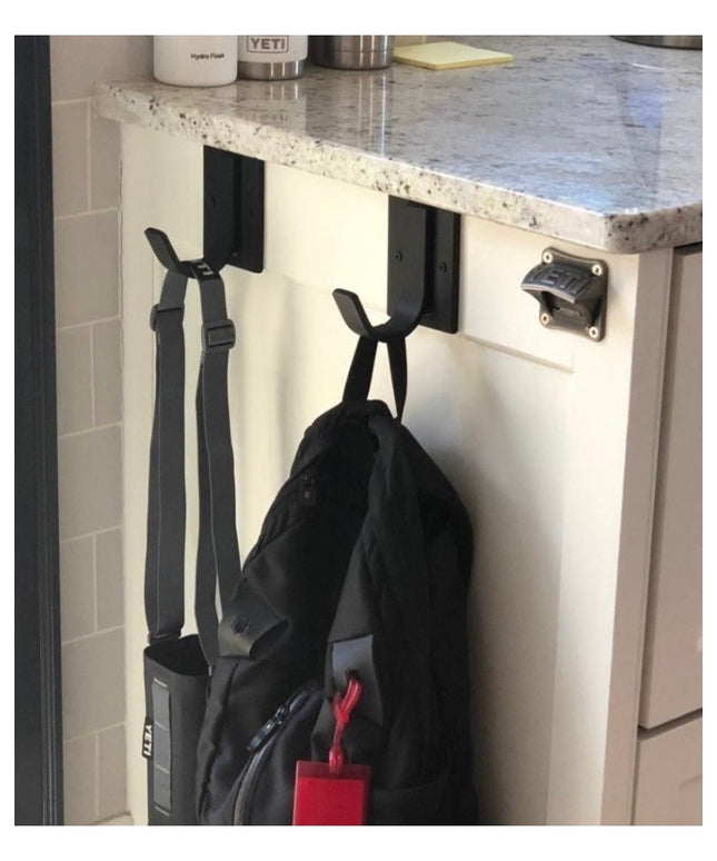 Black Dublin Mudroom Hook by Industrial Farm Co mounted on white kitchen cabinet door holding backpack and straps