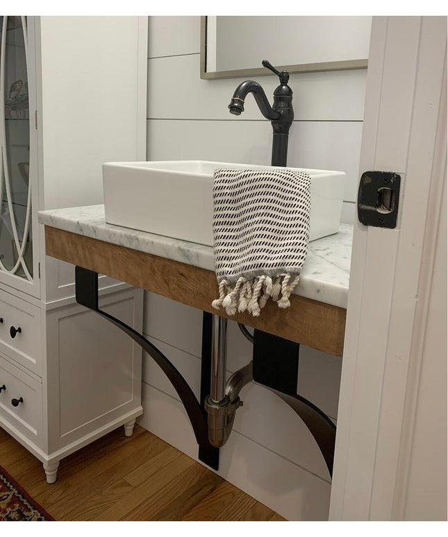 Black metal Rochester countertop support brackets holding wooden floating vanity with white vessel sink in modern farmhous...