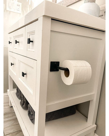 The Mitz black metal toilet paper holder by Industrial Farm Co mounted on white farmhouse bathroom vanity with open shelving