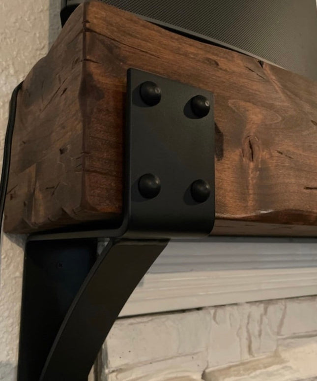Heavy duty black steel Spafford mantel bracket with decorative rivets supporting reclaimed wood beam above white brick fir...