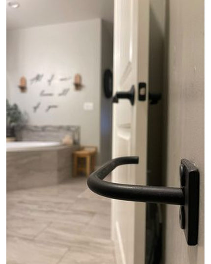 Black curved handle door hardware on white door frame with modern bathroom featuring bathtub visible in background - The M...