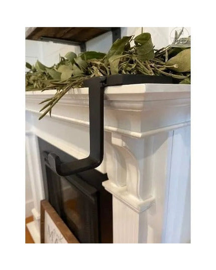 Black metal Annie Stocking Holder by Industrial Farm Co mounted on white fireplace mantel with greenery garland decoration