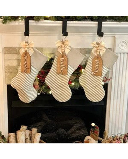 Black metal Annie Stocking Holder by Industrial Farm Co displaying three cream striped Christmas stockings with brown name...