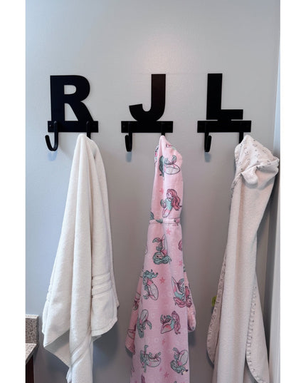 Black metal letter wall hooks R J L mounted on white wall with towels hanging from double hooks below each personalized mo...