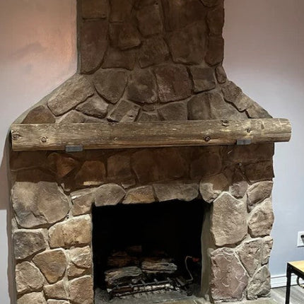 Stone fireplace with wooden mantel in a room with gray walls and tiled floor.