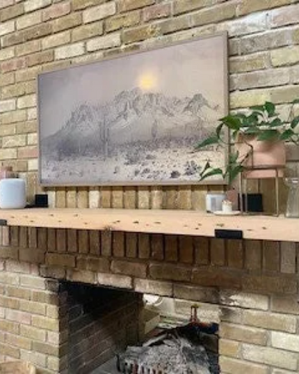 Brick fireplace with wooden mantel, decorative items, and a mountain painting.