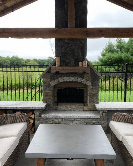 Outdoor patio with stone fireplace, cushioned furniture, and a scenic view.