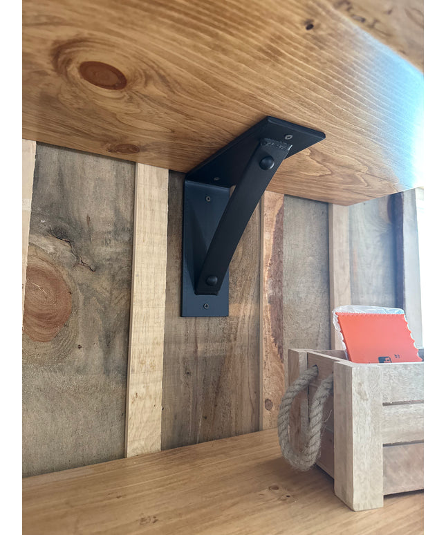 Wooden shelf with black metal bracket against a wooden wall.