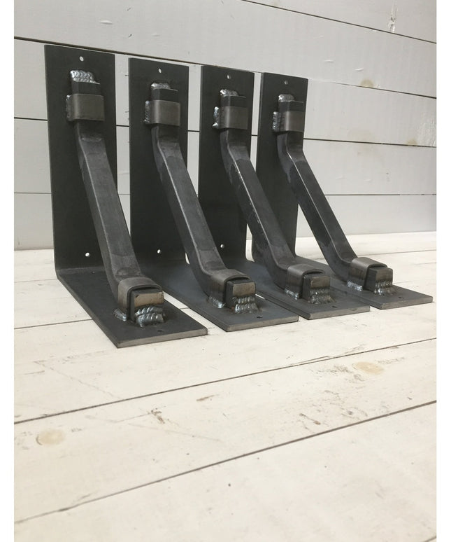 Four black metal Hornell Industrial Shelf Support brackets from Industrial Farm Co displayed on white wooden planks, showi...