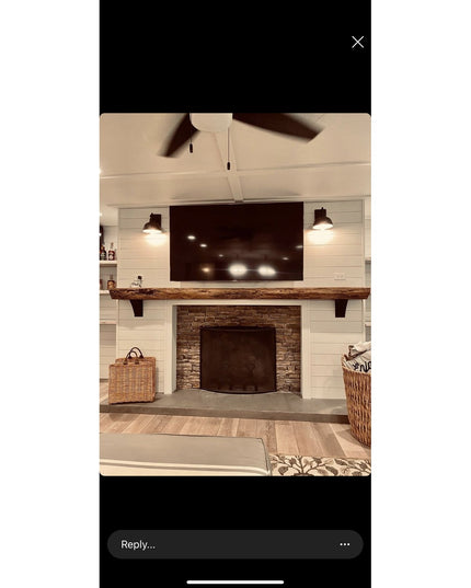 Rustic wooden mantel with dark metal Tipp Hill brackets supporting live-edge wood shelf above stone fireplace in modern fa...
