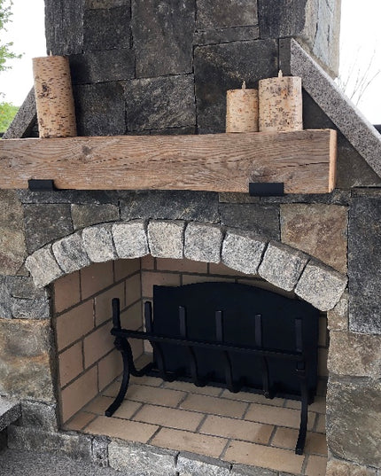 Stone outdoor fireplace with wooden mantel and black metal fire pit