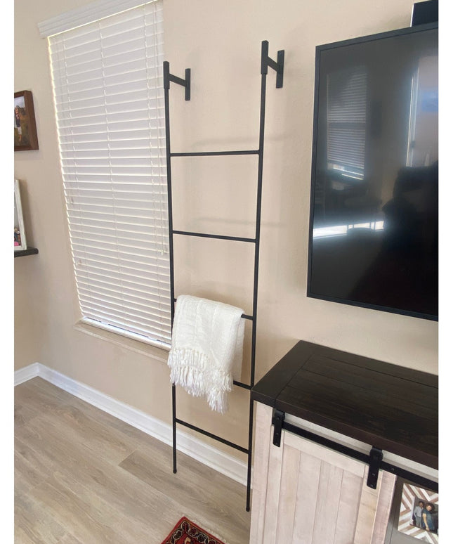 Black metal Brielle Top Mounted Blanket Ladder by Industrial Farm Co mounted on beige wall with white throw blanket in mod...