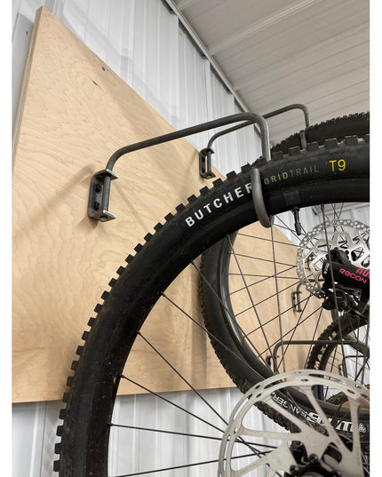 Logan Wall Mounted Bike Rack by Industrial Farm Co holding mountain bike wheel with Butcher tire against light wood plywoo...