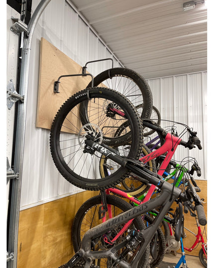 The Logan Wall Mounted Bike Rack by Industrial Farm Co holding multiple mountain bikes vertically against garage wall with...
