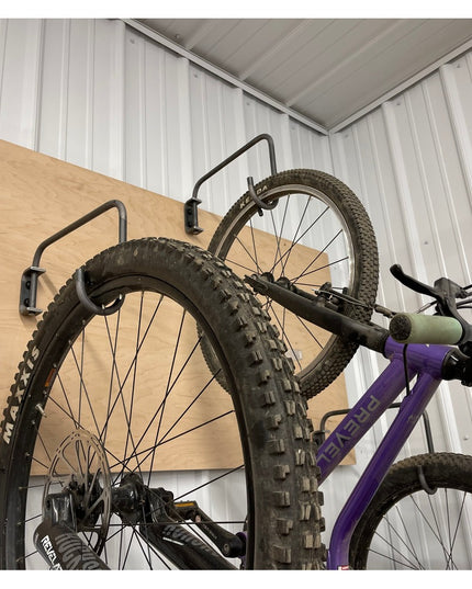 Purple mountain bike hanging on Logan Wall Mounted Bike Rack with black metal hooks and natural wood backing in garage sto...