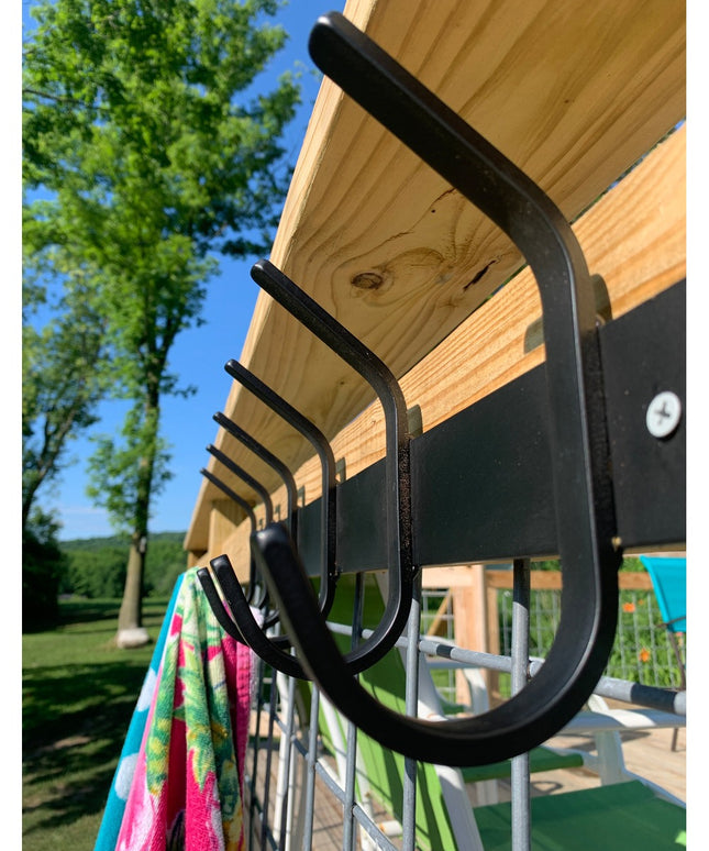 Black metal Eastman Coat & Hook Rack mounted under wooden pergola with colorful towel hanging, showing curved hook design