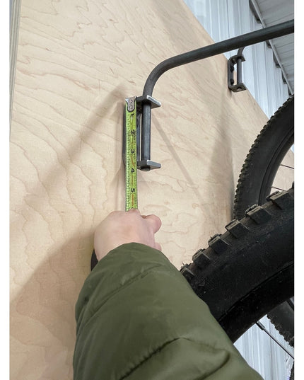 Person measuring black metal Logan Wall Mounted Bike Rack by Industrial Farm Co with green measuring tape on light wood wall