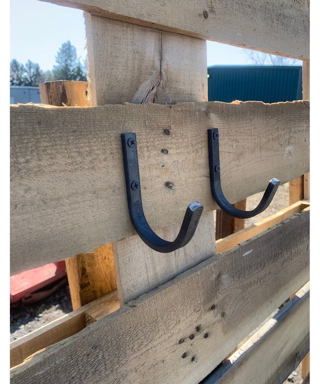 Two black metal Kenny wall hooks mounted on weathered wood beam, showing curved U-shaped design with visible screws from I...