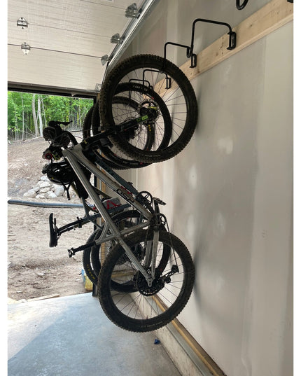 Black Logan Wall Mounted Bike Rack by Industrial Farm Co holding two mountain bikes vertically in white garage