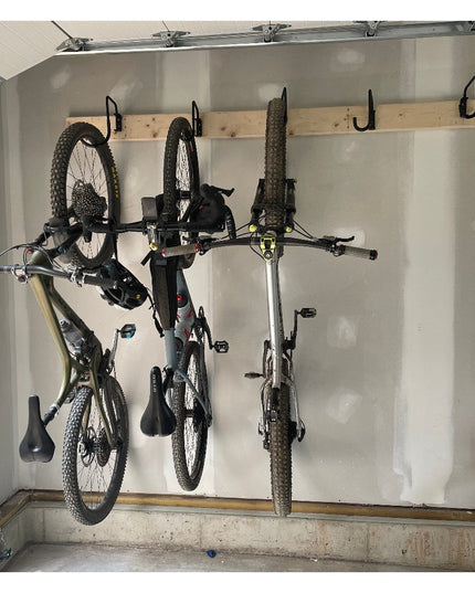 Industrial Farm Co Logan Wall Mounted Bike Rack with wooden rail and black metal hooks holding three mountain bikes in garage