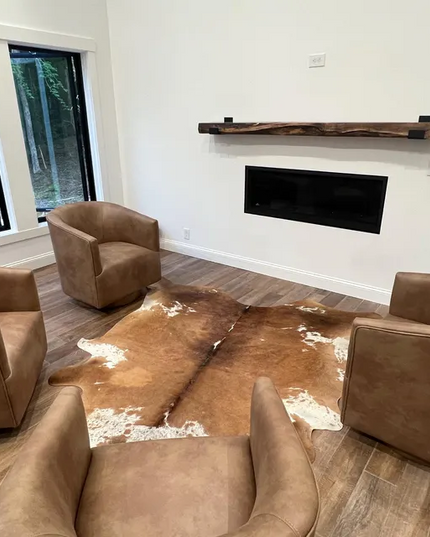 Living room with brown leather chairs and a cowhide rug in front of a white wall with a fireplace.