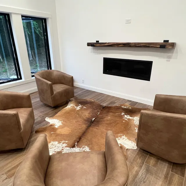Living room with brown leather chairs and a cowhide rug in front of a white wall with a fireplace.