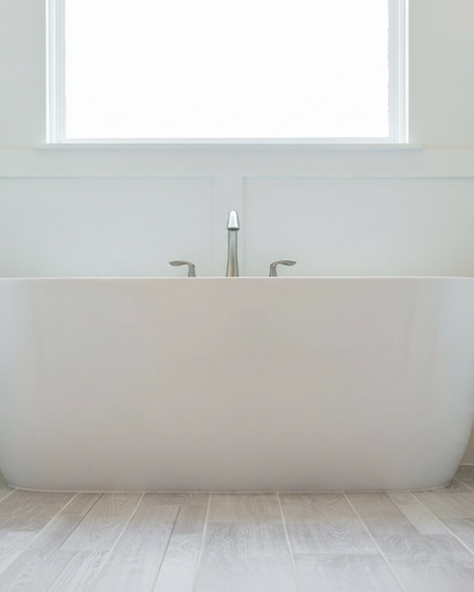 Modern white freestanding bathtub in a minimalistic bathroom with a window above.