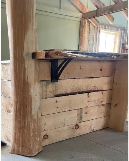 Black metal Jamestown 4-inch wide shelf bracket supporting wooden shelf in rustic farmhouse interior with exposed beams