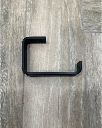 Black minimalist toilet paper holder from Industrial Farm Co mounted on light wood grain wall showing clean geometric L-sh...