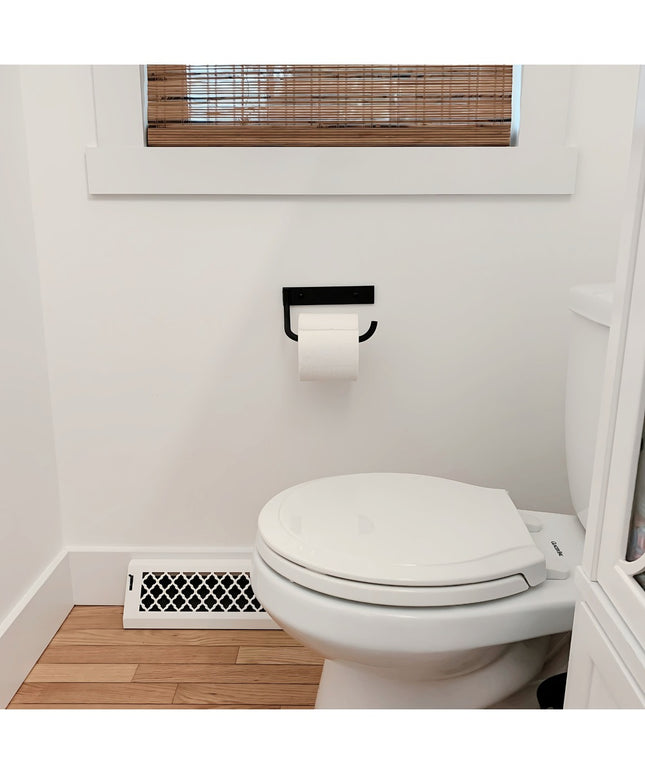 The Howlett Hill black metal toilet paper holder by Industrial Farm Co mounted on white bathroom wall with white toilet an...