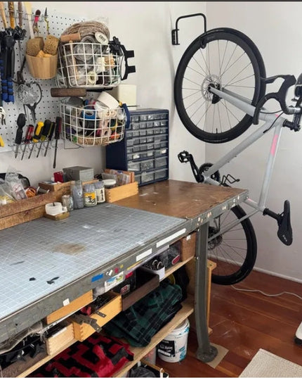 White Logan Wall Mounted Bike Rack by Industrial Farm Co holding gray bicycle in organized garage workshop with pegboard t...