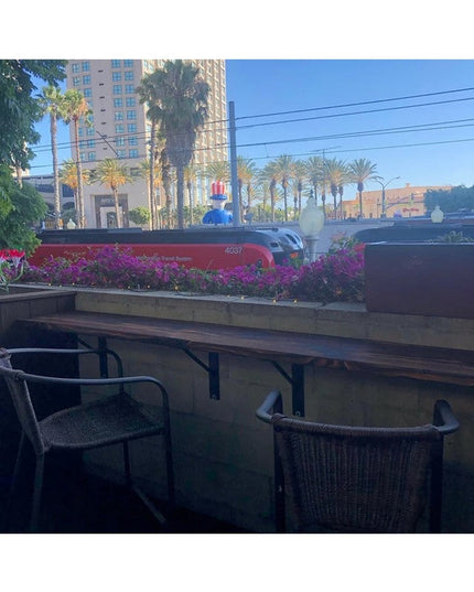 Black metal Oneida shelf brackets supporting wooden table surface with wicker chairs, train and palm trees visible in back...