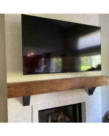 Rustic wooden mantel shelf mounted on white brick fireplace wall with black metal Tipp Hill Mantel Support brackets, TV mo...
