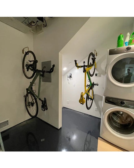 The Logan Wall Mounted Bike Rack by Industrial Farm Co holding two bicycles vertically on white walls in a modern laundry ...
