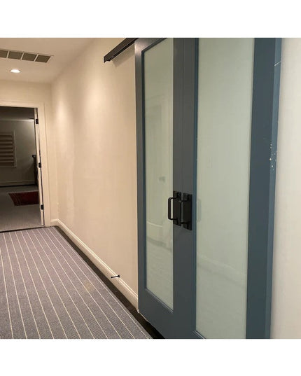 Black Lockport Pull door handle by Industrial Farm Co installed on frosted glass sliding doors in modern office hallway